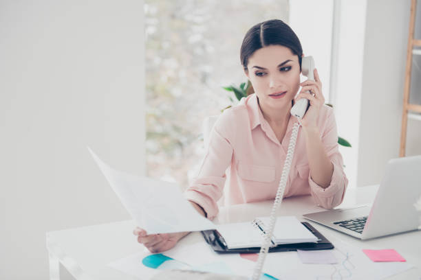 istock Concentrated secretary classic elegant financier making consultation looking at document in hand agent talking on telephone with partner consulting sitting in modern white office expertising analyzing 971015220