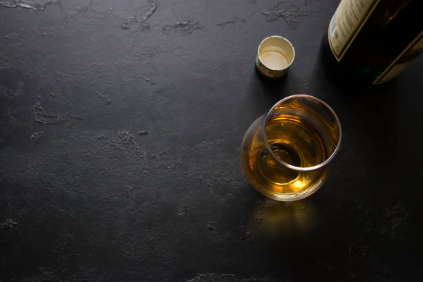 una bottiglia e un bicchiere di whisky su sfondo nero con spazio per il testo - tipping over foto e immagini stock