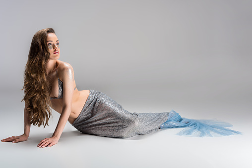 attractive woman with mermaid tail sitting on floor and looking away