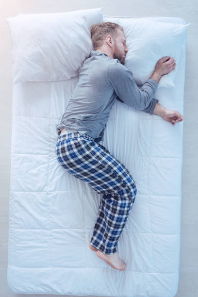 Tired millennial man falling asleep after working hard Recharging my batteries. Top view on a young man wearing pajamas taking a nap and sleeping tight after getting tired at home. man sleeping top view stock pictures, royalty-free photos & images