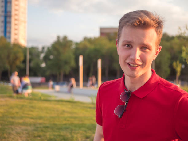 young smiling beautiful guy in red top walking in the park copy space