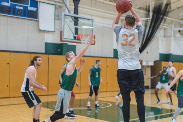 College Basketball Practice A men's college basketball team scrimmages in the gym. A left-handed player is shooting a three-pointer as a defender leaps out to try and block him. college basketball court stock pictures, royalty-free photos & images