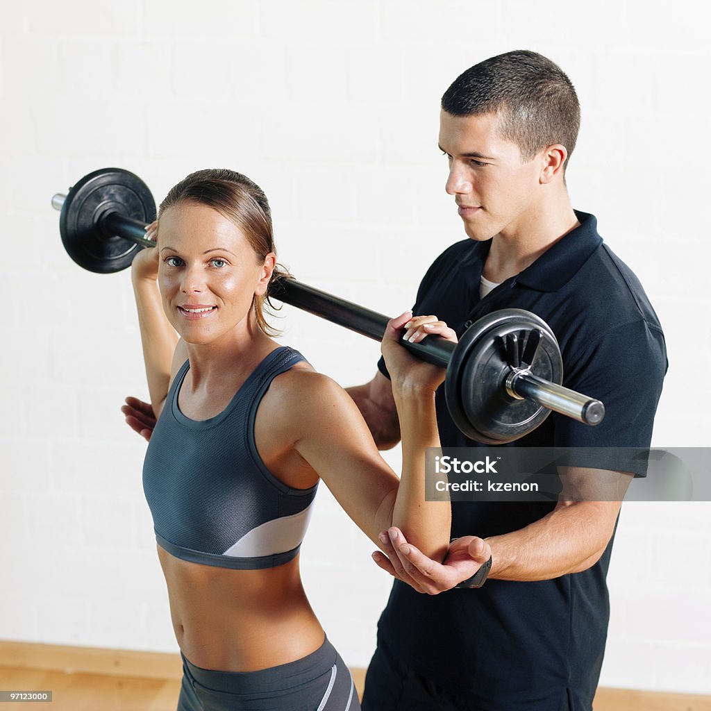 Male personal trainer helping a smiling female lift weights Woman with her personal fitness trainer in the gym exercising power gymnastics with a barbell Adult Stock Photo