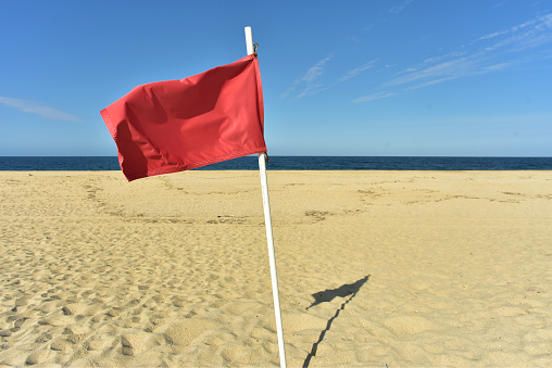 red flag flying in wind on flag pole on sand beach with blue sky