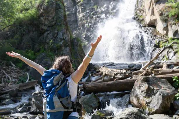 Photo of A girl is standing with a backpack near a waterfall.