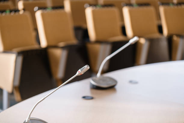 istock microphone in the foreground. Seminar presentation. Conference room full of empty seats. Red color. Hall for workshops and seminars 971304928