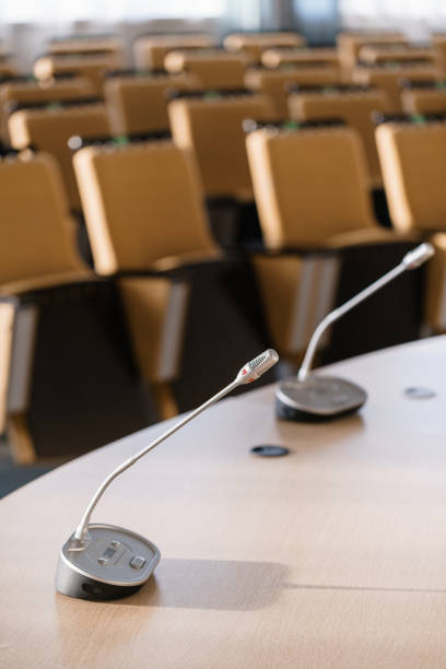 istock microphone in the foreground. Seminar presentation. Conference room full of empty seats. Red color. Hall for workshops and seminars 971305072
