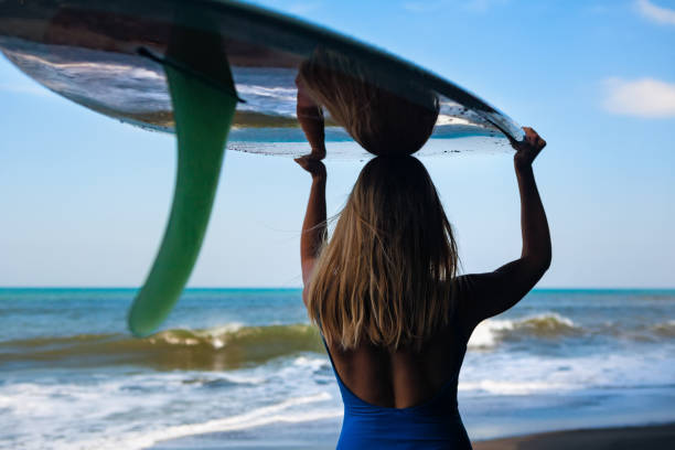 istock Young woman with surfboard walk on black sand beach 971325486