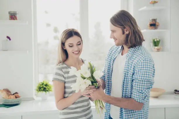 Portrait of trendy stylish couple enjoying holiday together, handsome man giving bouquet of white tulips to lover making surprise. Daydream delight lovestory concept