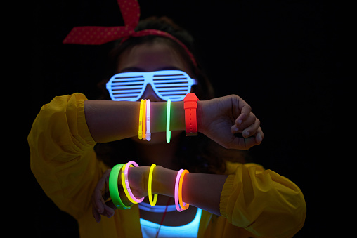Cheerful young woman with neon bracelets in dark room