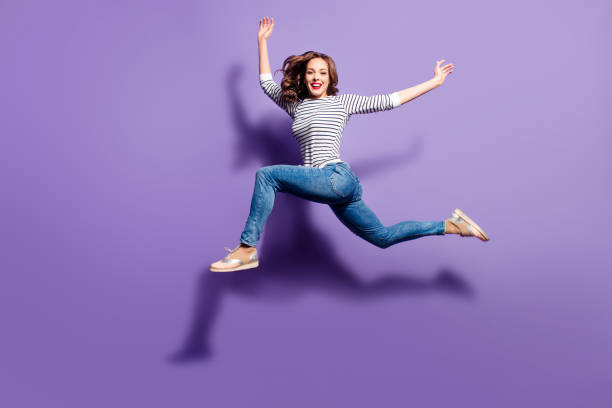 retrato de niña tonta loca saltando por encima en el aire mirando a cámara con buen estiramiento aislado sobre fondo violeta, concepto de estilo de vida de energía de la vida de personas - jumping women running vitality fotografías e imágenes de stock