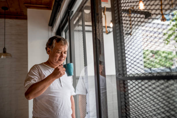 istock Senior asian man standing by the window and holding a mug 971399698