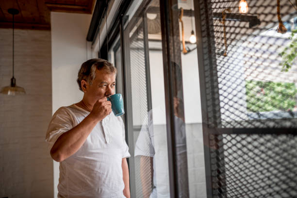 istock Senior asian man standing by the window and drinking from a mug 971399726