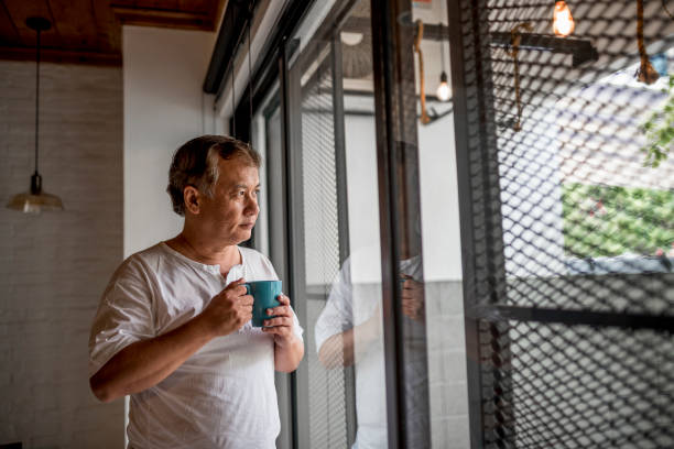 istock Senior asian man looking through the window and holding a mug 971399732