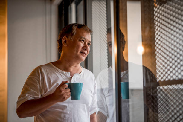 istock Senior asian man looking through the window and holding a mug 971399876
