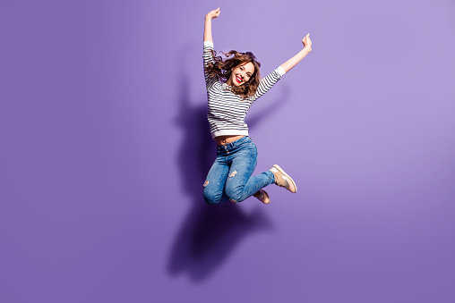Retrato de muchacha positiva alegre saltando en el aire con los puños levantados mirando a cámara aislada sobre fondo violeta. Concepto de energía de personas de la vida photo