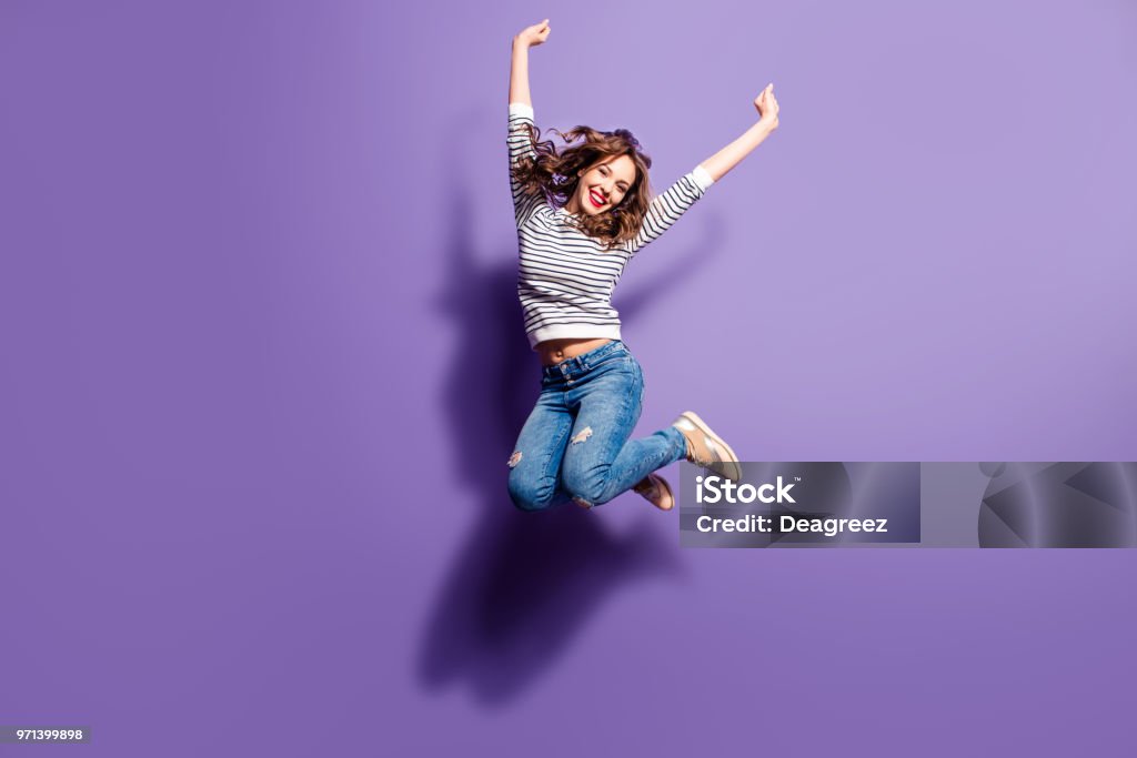 Portrait of cheerful positive girl jumping in the air with raised fists looking at camera isolated on violet background. Life people energy concept Women Stock Photo