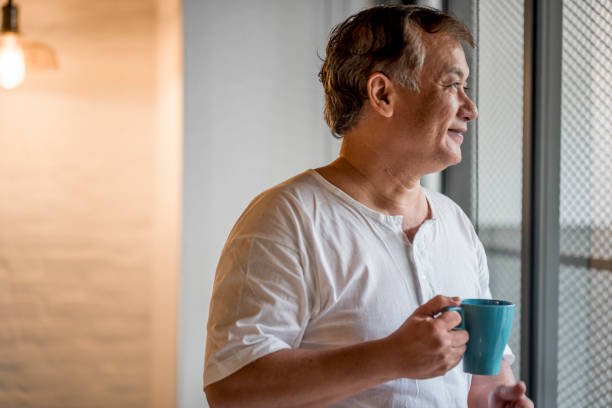 istock Senior asian man looking through the window and holding a mug 971400046