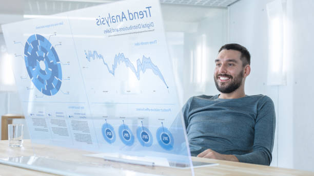istock In the Near Future Successful Smiling Trader Works on Computer with Transparent Display that Shows Interactive Line Charts and Other Useful Information. His Office is Bright and Modern. 971403510