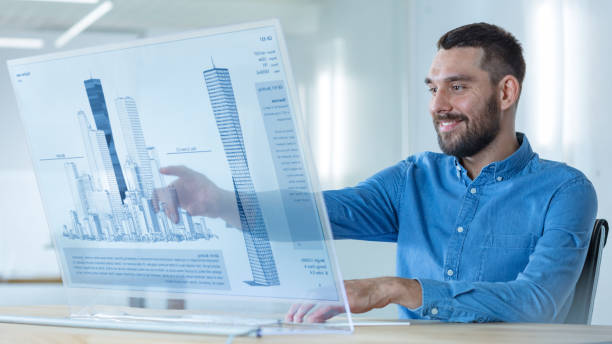 In the Futuristic Office Male Architects Works on the Transparent Computer Display with Skyscraper Building Model. Technologically Advanced Office Professional People Use 3D Modeling Software Application. en la futurista oficina arquitectos hombre trabaja en la pantalla de computadora transparente con el modelo de construcción de rascacielos. oficina de tecnología avanzada profesional personas utiliza aplicación de software de modelado 3d.