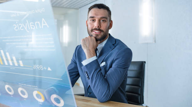 istock In the Near Future Successful Businessman Works on Computer with Transparent Display that Shows Stock Market Analyzing Data, Pie Charts, Rises and Downs. 971403598