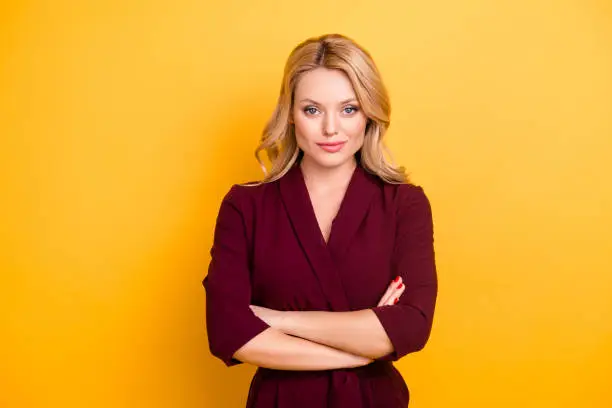 Portrait of pretty charming  woman in burgundy suit having her arms crossed looking at camera isolated on yellow background