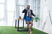businessman in jacket and shorts talking on smartphone at workplace in office