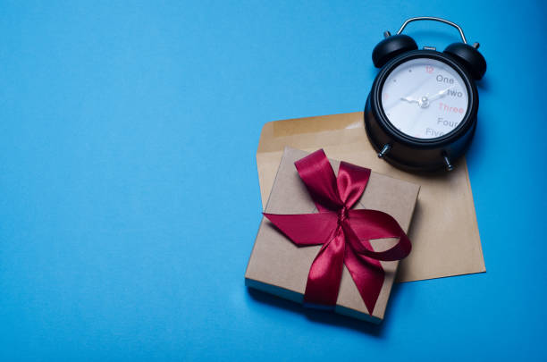 istock Alarm clock, envelope and gift box with red ribbon on a blue background. Top view, copy space 971433732