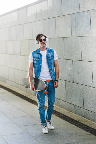 istock smiling young skateboarder in headphones with longboard 971444450