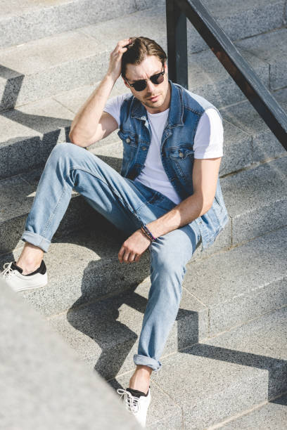 istock handsome young man sitting on stairs and looking away 971448380