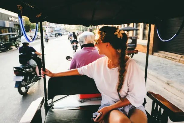 Woman on the road trip by rickshaw meets bright tropical sunset in Siem Reap