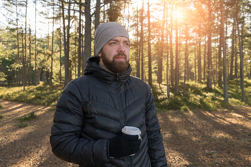 Caucasian bearded man with take away cup of coffee walking in forest and enjoys privacy. Take a break concept, toned