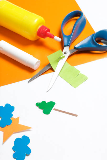 istock Lessons in applique. Necessary items: glue, colored paper and scissors lie on the white surface of the table. Cut several elements. 971503764
