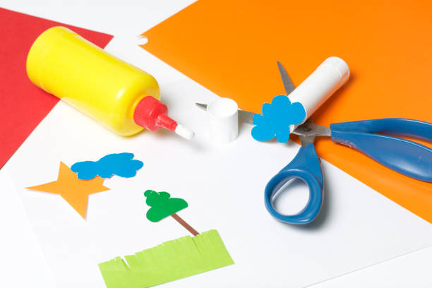 istock Lessons in applique. Necessary items: glue, colored paper and scissors lie on the white surface of the table. Cut several elements. 971503828