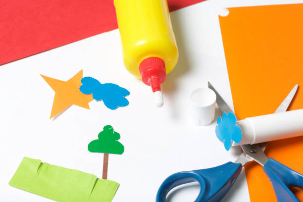 istock Lessons in applique. Necessary items: glue, colored paper and scissors lie on the white surface of the table. Cut several elements. 971503866