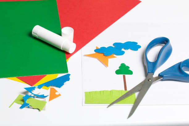 istock Lessons in applique. Necessary items: glue, colored paper and scissors lie on the white surface of the table. Cut several elements. 971503880