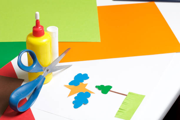 istock Lessons in applique. Necessary items: glue, colored paper and scissors lie on the white surface of the table. Cut several elements. 971503928