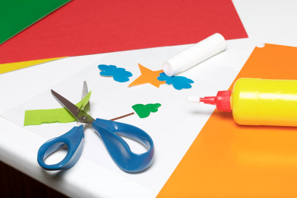 istock Lessons in applique. Necessary items: glue, colored paper and scissors lie on the white surface of the table. Cut several elements. 971503950