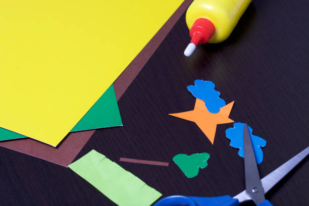 istock Lessons in applique. Necessary items: glue, colored paper and scissors lie on the dark surface of the table. Cut several elements. 971544954