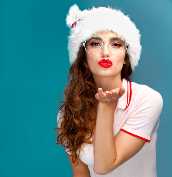 Studio portrait of a beautiful young woman blowing a kiss while wearing a Christmas hat against a blue background
