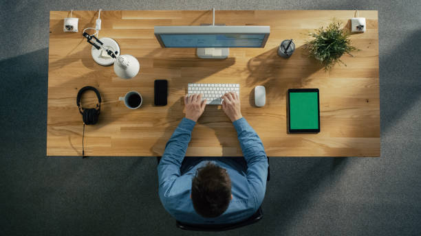 istock Top View of a Software Engineer Typing on His Desktop Computer. Tablet Computer and Smartphone with Green Screen Lying on the Table. 971549188