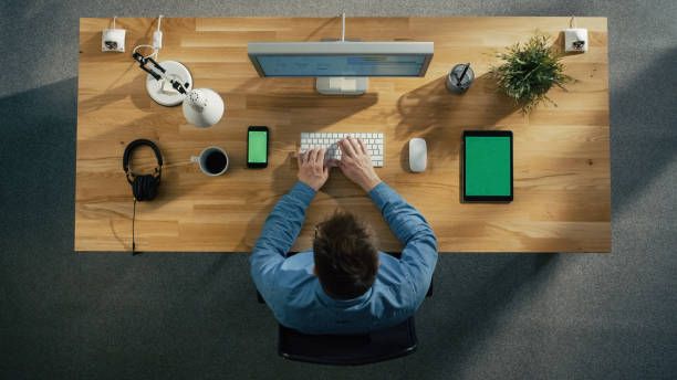 istock Top View of a Software Engineer Working at His Desktop Computer Sitting in His Creative Office. Lying on the Table: Smartphone, Tablet Computer, Headphones. 971549192