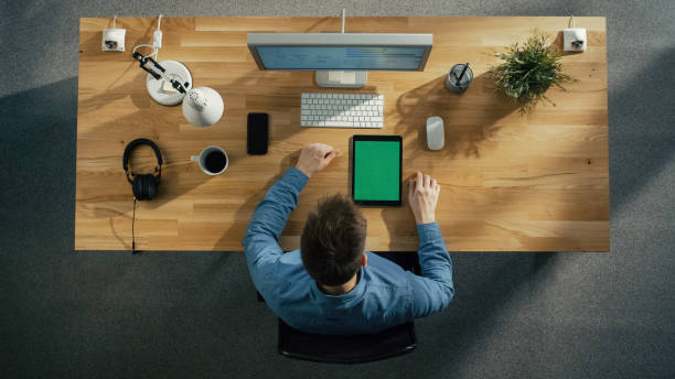 istock Top View of a Software Engineer Typing on His Desktop Computer. Tablet Computer and Smartphone with Green Screen Lying on the Table. 971549214