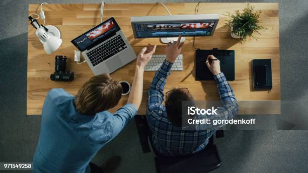 Top View Of Two Young Talented Photographers Discussing Footage One Of Them Works On A Digital Drawing Tablet At His Desktop Computer Processing Wedding Photography His Workplace Is Covered With Sunlight Stock Photo - Download Image Now