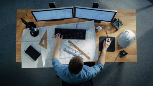 Top View of a Technical Engineer Working on His Blueprints, Drawing Plans, Using Desktop Computer. Various Useful Items Lying on his Table. Top View of a Technical Engineer Working on His Blueprints, Drawing Plans, Using Desktop Computer. Various Useful Items Lying on his Table. engineer stock pictures, royalty-free photos & images