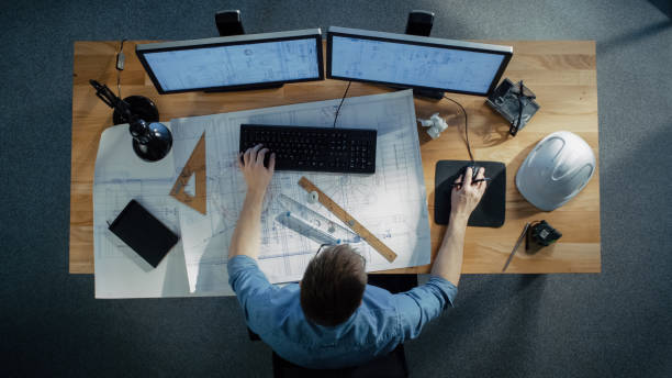 Top View of a Technical Engineer Working on His Blueprints, Drawing Plans, Using Desktop Computer. Various Useful Items Lying on his Table. Top View of a Technical Engineer Working on His Blueprints, Drawing Plans, Using Desktop Computer. Various Useful Items Lying on his Table. architecture project stock pictures, royalty-free photos & images