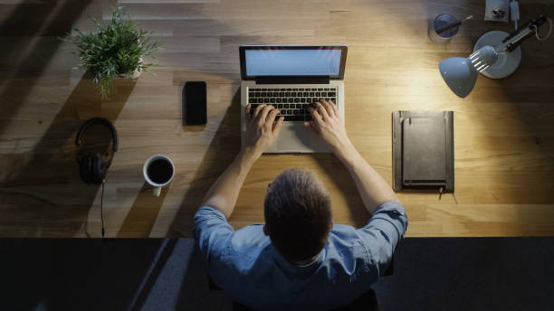 istock Top View of Young Creative Designer Working on His Laptop at Night. He Drinks Coffee. Table Light Turned On. 971549358