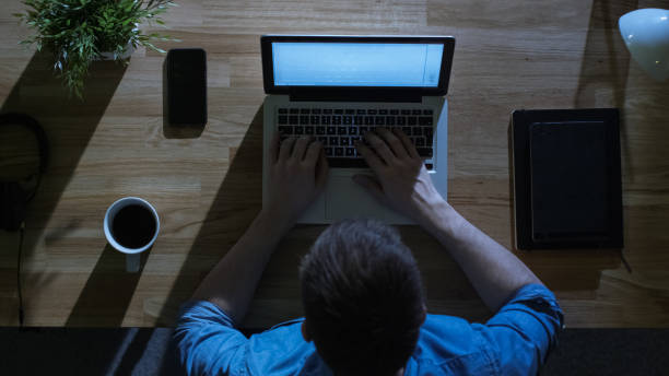 istock Top View of Creative Designer Working on His Laptop at Night. His Table is Illuminated by Cold Blue Light From Outside. 971549364