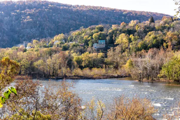 Harper's Ferry blue Potomac River riverside with colorful orange yellow foliage fall autumn by small village town in West Virginia, WV, house on hill mountain