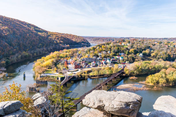 Harper's Ferry overlook closeup of cityscape with cliffs rocks, colorful orange yellow foliage fall autumn forest with small village town by river in West Virginia, WV Harper's Ferry overlook closeup of cityscape with cliffs rocks, colorful orange yellow foliage fall autumn forest with small village town by river in West Virginia, WV harpers ferry photos stock pictures, royalty-free photos & images